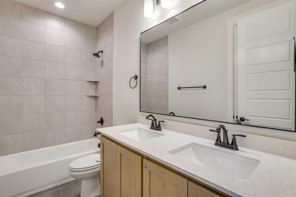 Double vanity with light wood cabinetry, white stone-finish countertops, undermount rectangular sinks, large frameless mirror, and matte black fixtures throughout