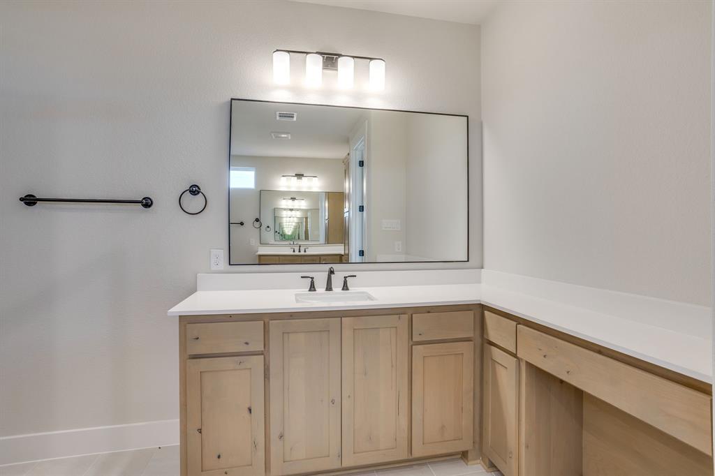 Wood-finish cabinetry featuring an extended vanity counter, a rectangular integrated sink, a large framed mirror, and matte black hardware