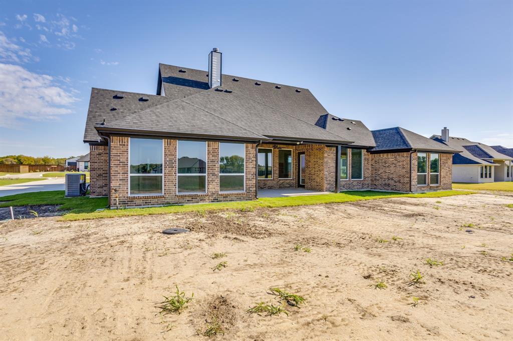 Multi-faceted brick exterior featuring a shingle roof, chimney, expansive rear windows, and a covered patio