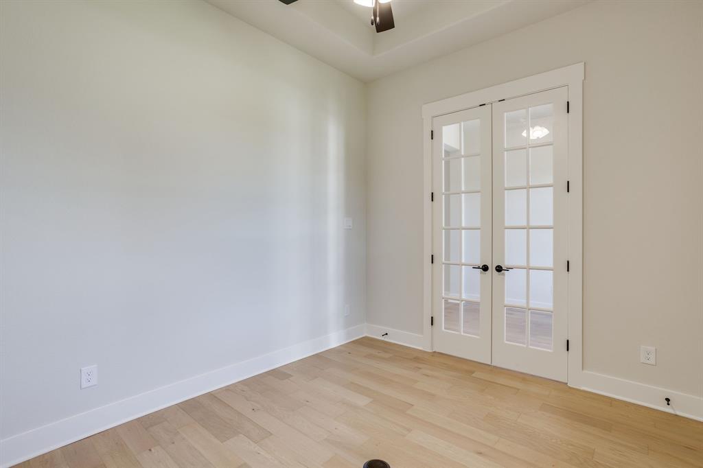 Tray ceiling featuring a central ceiling fan, light-toned wood-finish flooring, and white double French doors with glass panes and dark hardware