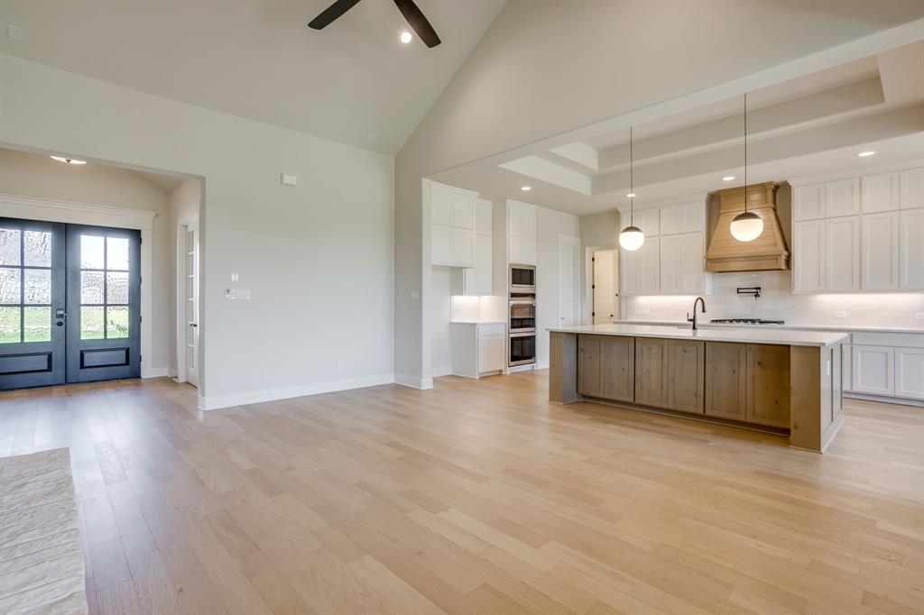 Vaulted ceilings with recessed lighting, wood-finish flooring, double-entry doors, kitchen island with wood-finish cabinetry, and custom range hood