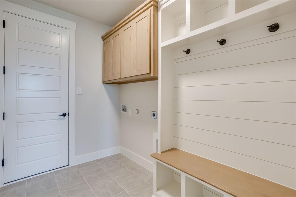 Built-in mudroom bench with shelving, light wood-finish cabinetry, white horizontal shiplap wall detailing, tile flooring, and a five-panel interior door with matte black hardware