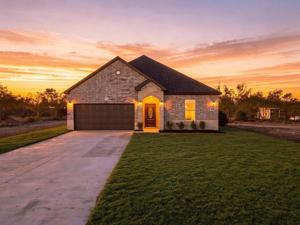 Single-story residence featuring a brick exterior, a covered entryway, a two-car garage, and an expansive front lawn
