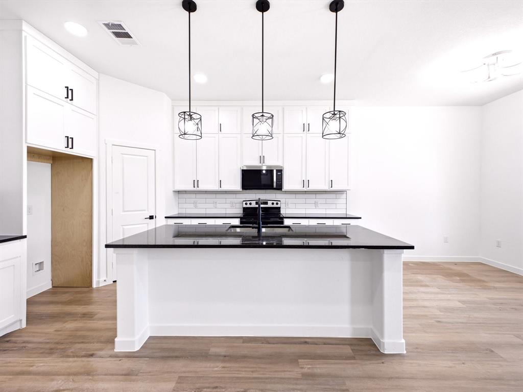Kitchen featuring white shaker-style cabinetry, a contrasting center island with a dark countertop, subway tile backsplash, and three black geometric pendant lights over a wood-finish floor