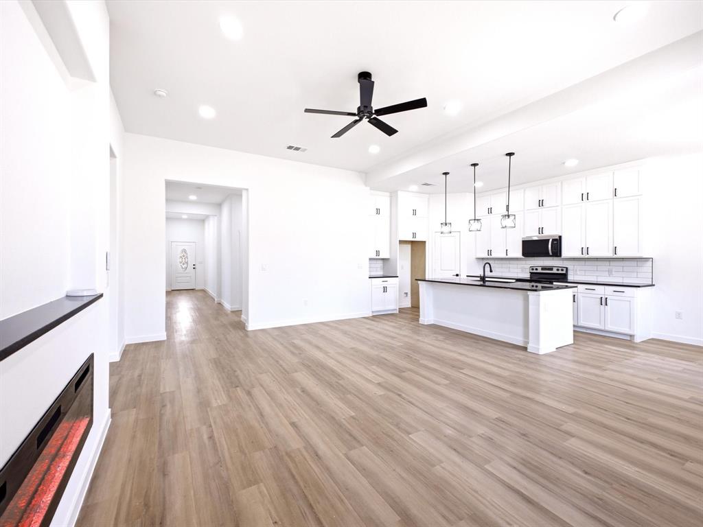Open-concept interior featuring wood-finish flooring, white cabinetry, a center island with a dark countertop, recessed lighting, and a built-in electric fireplace