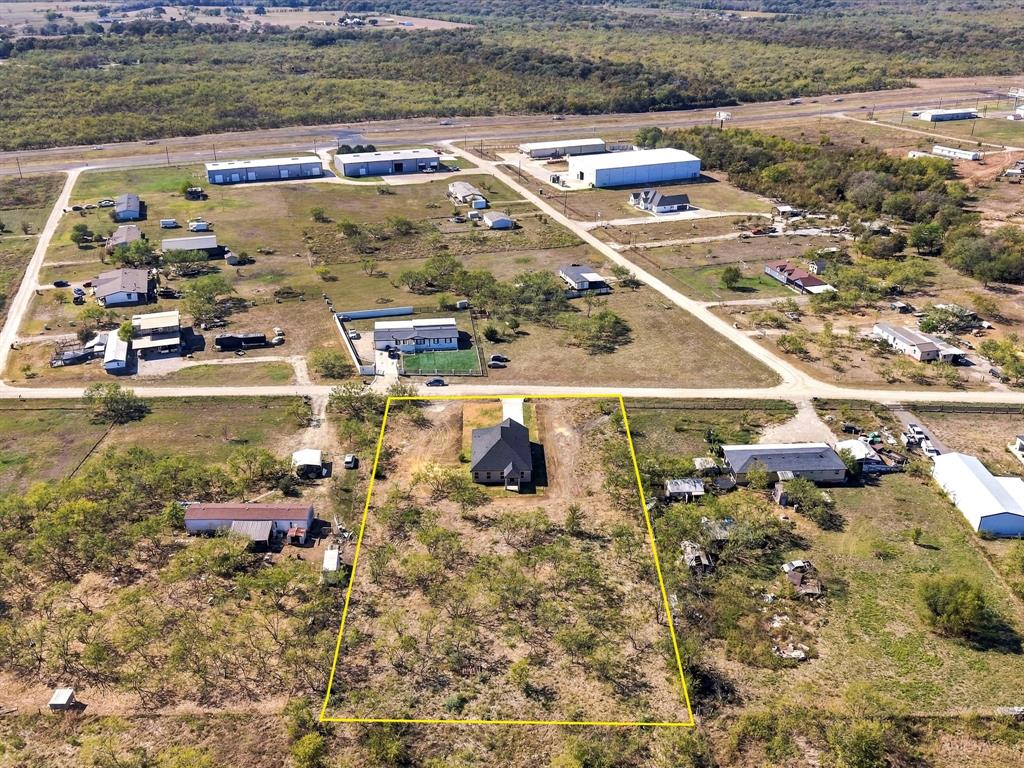 Aerial perspective of an expansive residential lot featuring mature trees, a concrete driveway, and a detached single-story residence with a dark-toned pitched roof