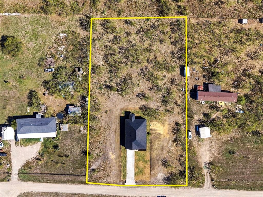 Aerial perspective of a rectangular parcel featuring a central structure with a dark shingled roof, a paved driveway, and natural landscape