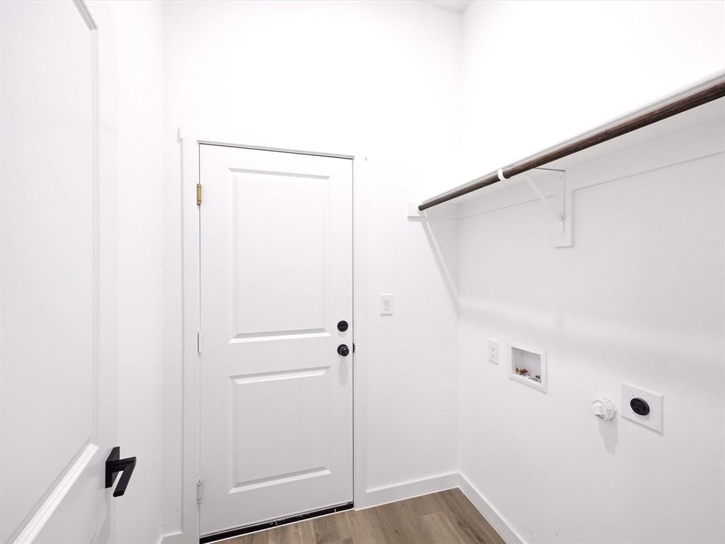 Utility area featuring wood-finish flooring, a solid-core paneled door with matte black hardware, built-in shelving with hanging rod, and dedicated washer and dryer hookups