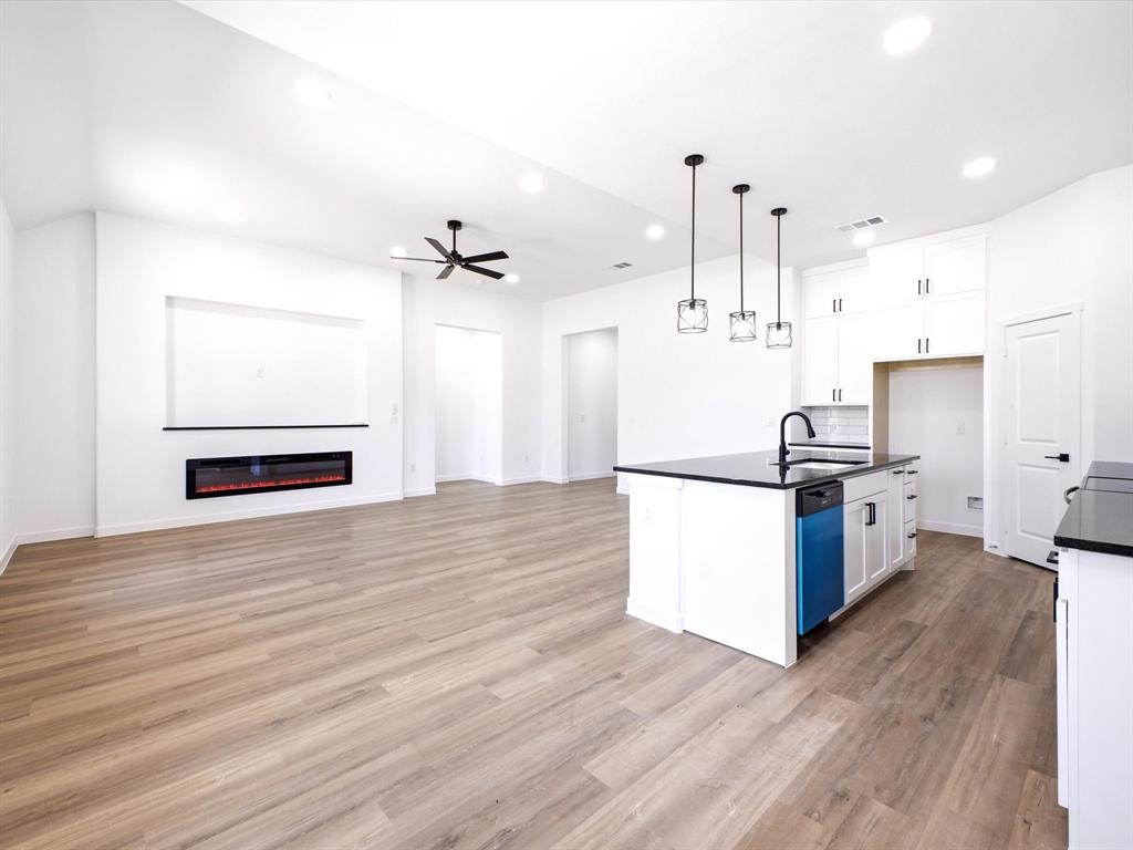 Open-concept interior featuring wood-finish flooring, a wall-mounted electric fireplace, a kitchen island with stone-surface countertops, recessed lighting, and pendant fixtures