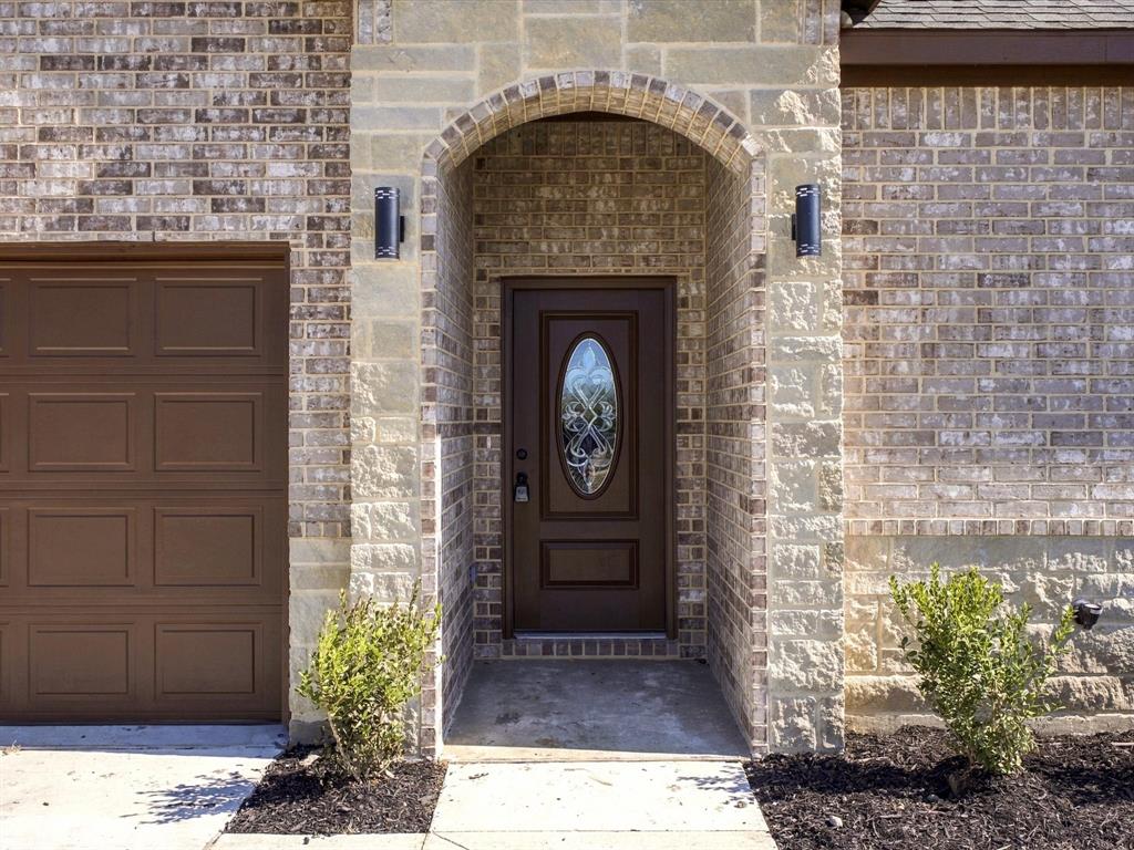 Brick and stone masonry facade featuring an arched entryway, recessed front door with an oval glass inlay, and dual wall-mounted exterior light fixtures