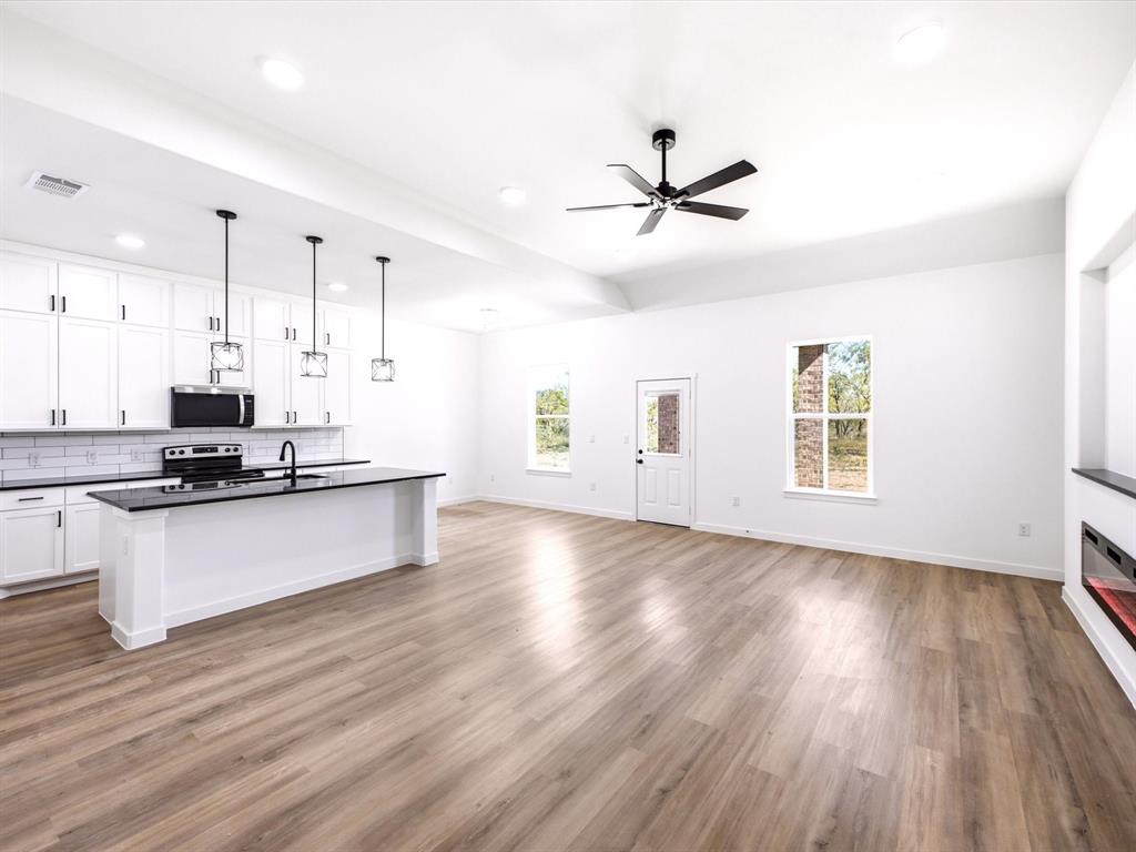 Open-concept kitchen featuring white shaker-style cabinetry, dark stone-finish countertops, a central island with pendant lighting, wood-finish flooring, and a built-in linear fireplace