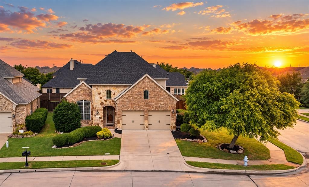 Multi-gabled brick and stone exterior featuring a two-car garage, concrete driveway, and manicured landscaping with mature trees