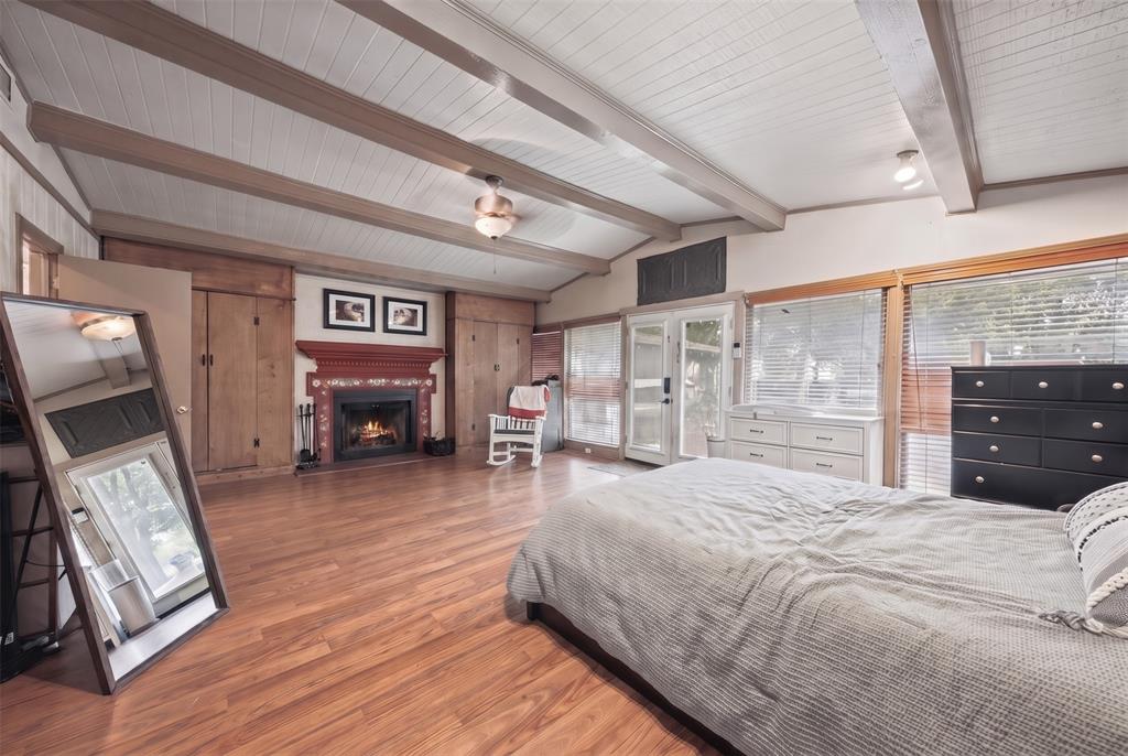 Vaulted ceiling with exposed wood-finish beams, wood-finish flooring, built-in wooden cabinetry, fireplace with a decorative mantle, and glass-paneled double doors