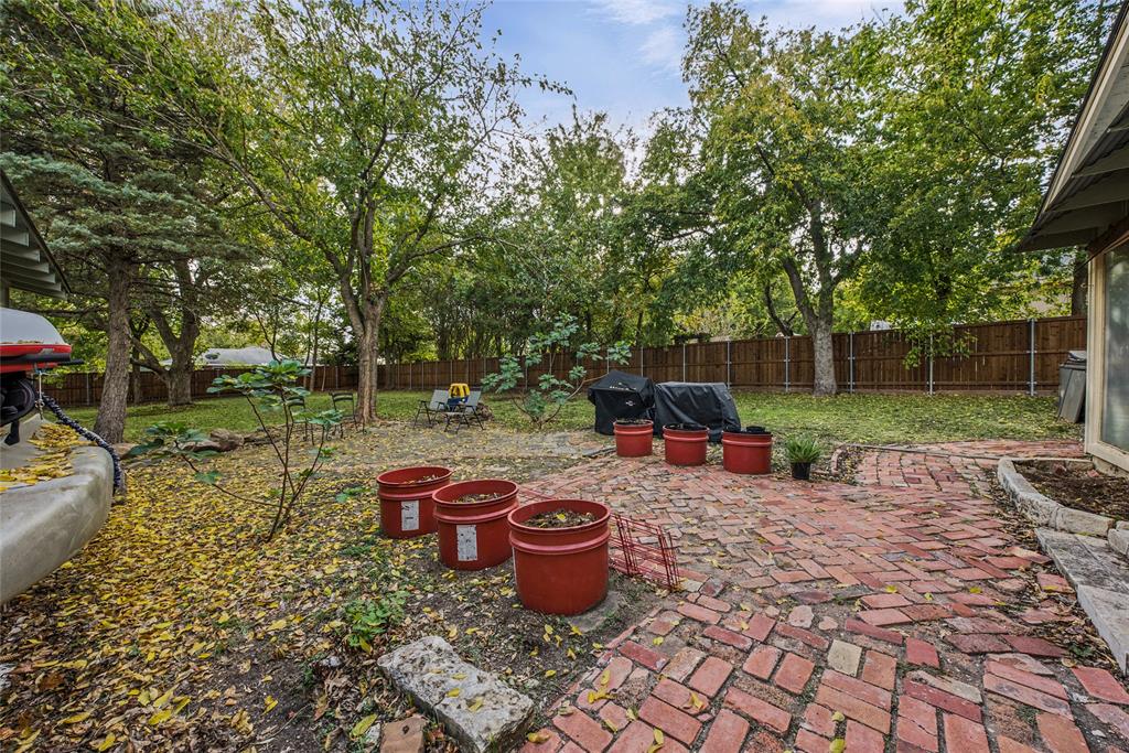 Expansive backyard featuring a brick paver patio, mature trees, and a wooden perimeter fence