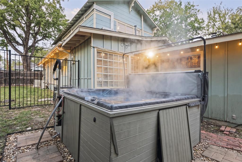 Outdoor space featuring an elevated hot tub with an integrated cover lift system, set on a stone-paver foundation within a fenced perimeter