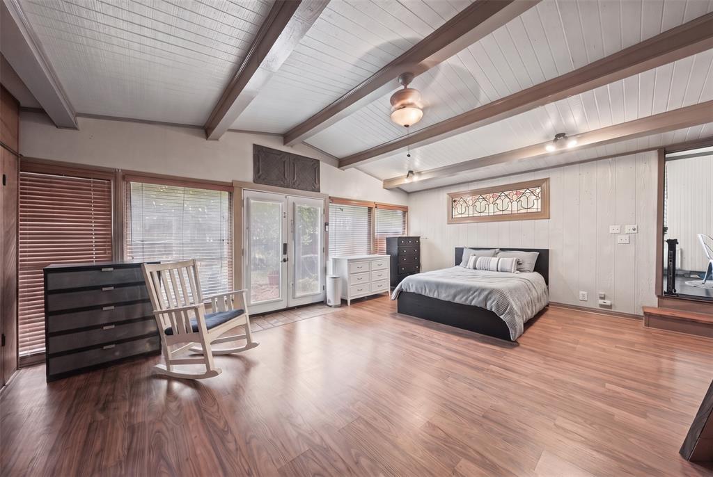Vaulted ceilings with exposed wooden beams, wood-finish flooring, dual glass-panel exterior doors, and an elongated decorative leaded-glass window