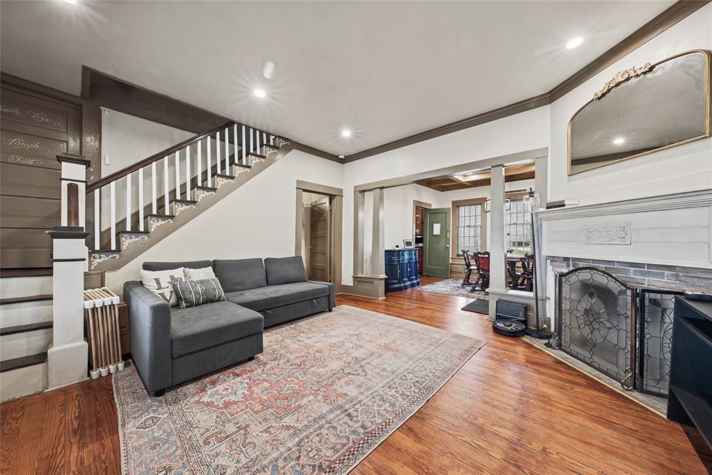 Staircase with white balusters and wood-finish handrail, fireplace with brick surround and decorative mantle, recessed lighting, and wood-finish flooring