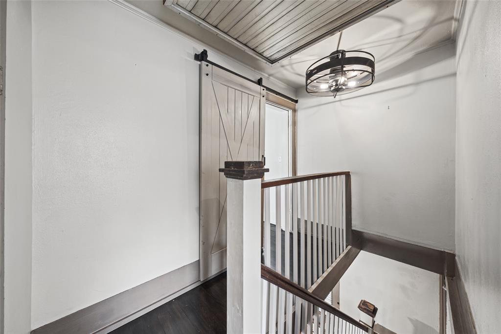 Sliding barn-style door, dark-toned flooring, white spindle railing, and a drum-style pendant light fixture