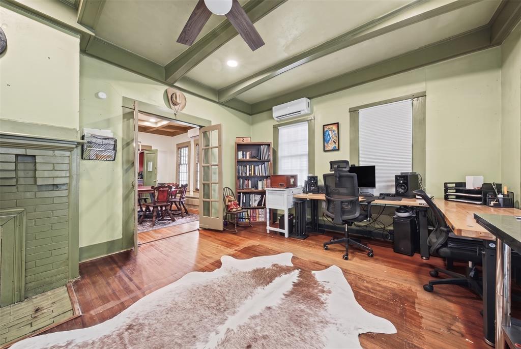 Room featuring hardwood flooring, beamed ceiling, painted brick fireplace, and dual-pane windows with trim casing