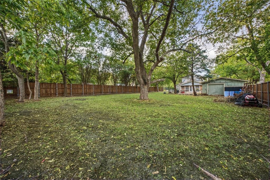 Expansive backyard featuring mature shade trees, a tall wood privacy fence, and a detached structure