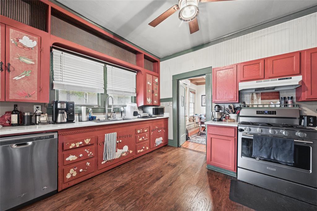 Kitchen featuring wood-finish flooring, custom cabinetry with integrated shelving, stainless steel dishwasher, gas range with hood, and beadboard wall paneling