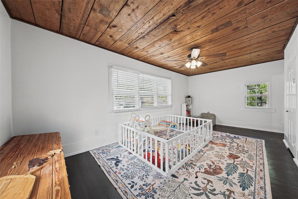 Room featuring a natural wood-plank ceiling, dark wood-finish flooring, multi-pane windows with horizontal blinds, and a central ceiling fan with integrated lighting