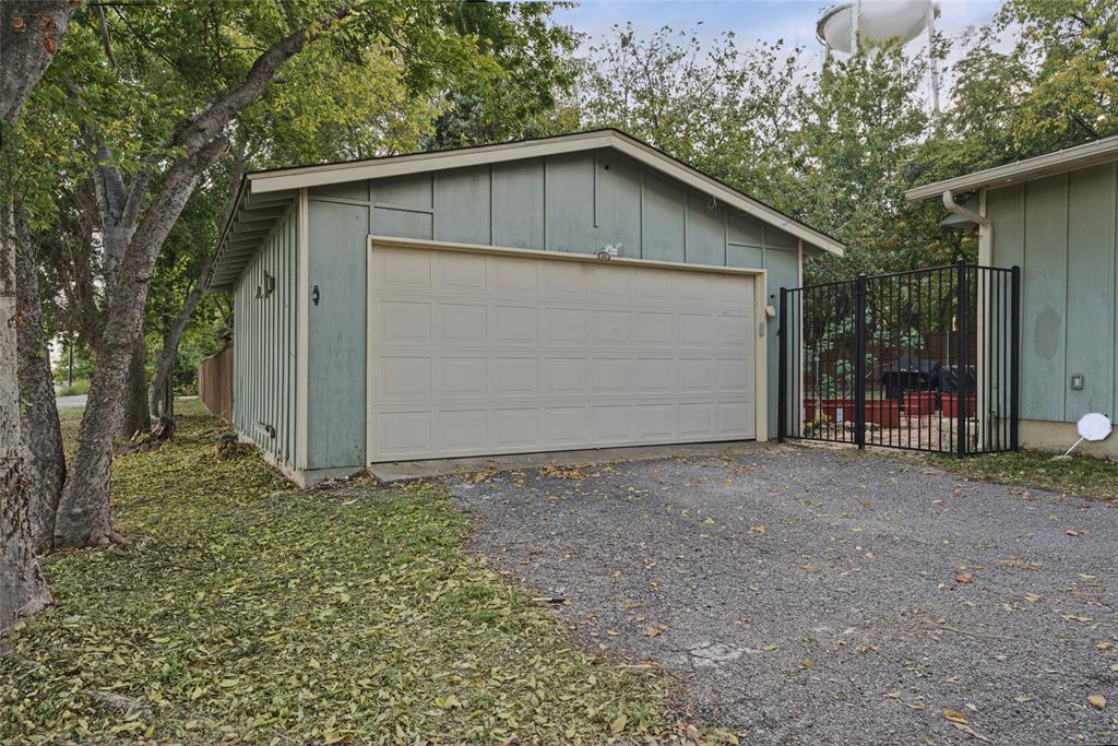 Detached two-car garage featuring vertical wood siding, a wide sectional garage door, gravel driveway, and a black metal perimeter fence