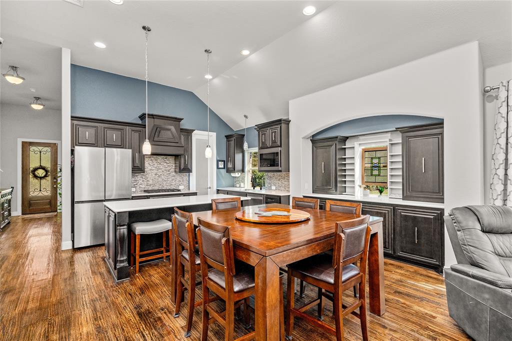 Vaulted ceilings, wood-finish flooring, custom dark cabinetry, stone-tile backsplash, and integrated buffet-style cabinetry with built-in shelving