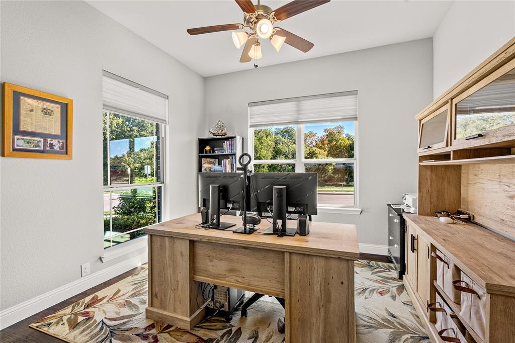 Room featuring wood-finish flooring, dual windows with integrated shades, a built-in wood-finish workstation, and a multi-light ceiling fan