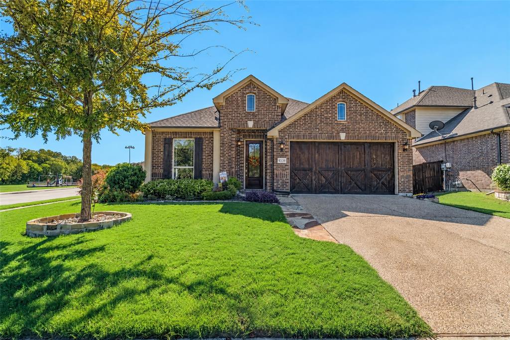 Brick exterior with a gabled roofline, decorative wood-finish garage door, and a manicured front lawn with a stone-bordered tree planter Brick exterior with a gabled roofline, decorative wood-finish garage door, and a manicured front lawn with a stone-bordered tree planter