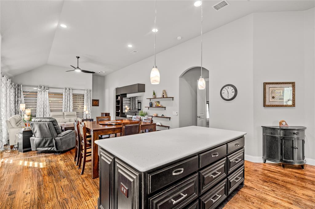 Vaulted ceiling featuring recessed lighting, a central kitchen island with a stone-finish countertop and dark cabinetry, and wood-finish flooring