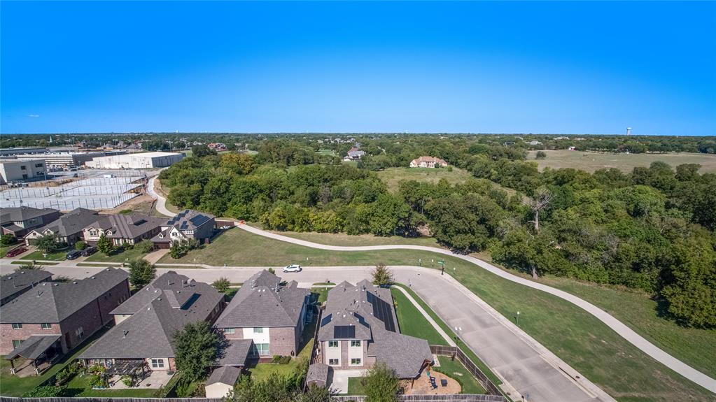 Aerial perspective featuring residential structures with solar panels, a paved multi-use pathway, and mature tree-lined green space