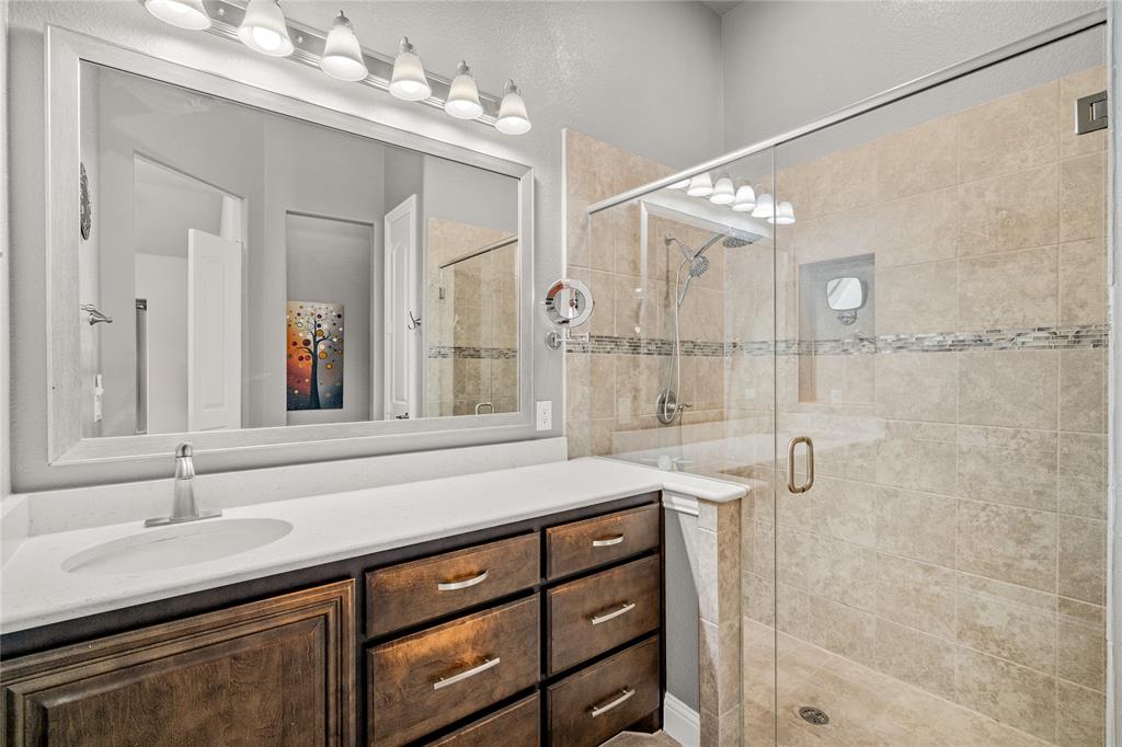 Bathroom featuring a wood-finish vanity with a solid-surface countertop, an expansive framed mirror, a multi-bulb vanity light, and a walk-in shower with tile surround and a glass door