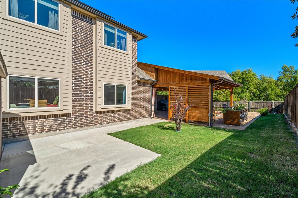 Exterior featuring a two-story brick and horizontal siding facade, a covered patio with a wooden privacy screen, a concrete slab, and a grass lawn