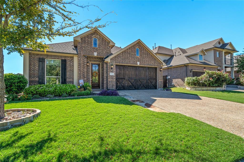 Brick exterior featuring a multi-gabled roofline, decorative wooden carriage-style garage doors, and a stone-aggregate driveway