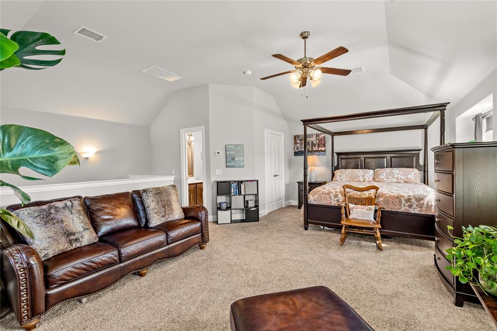 Vaulted ceiling with neutral wall tones, carpeted flooring, ceiling fan with light fixture, and wall-mounted sconce lighting