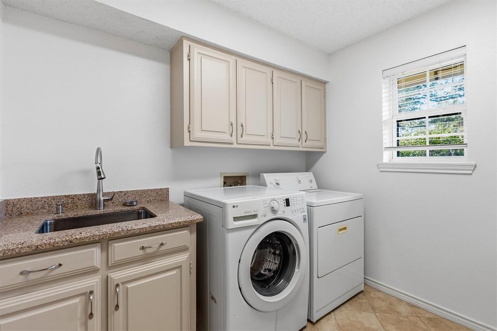 Laundry space featuring neutral-toned built-in upper and lower cabinetry, stone-finish countertop, integrated drop-in sink with a pull-down faucet, and ceramic tile flooring
