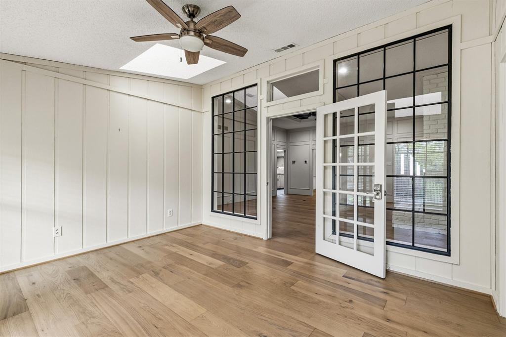 Board-and-batten wall detailing, wood-finish flooring, skylight, ceiling fan, and black-framed glass french doors