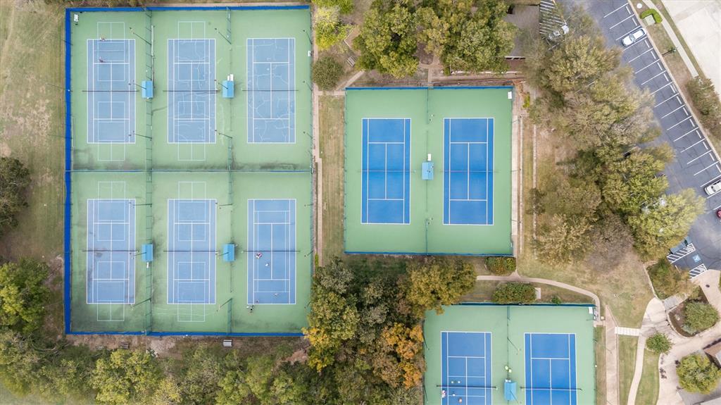 Aerial view featuring eight hard-surface tennis courts with perimeter fencing, stadium-style netting, and paved parking area