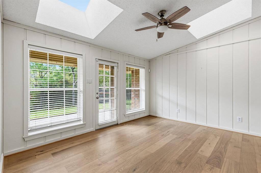 Wood-finish flooring, dual skylights, vertical paneling, and a ceiling fan in a room with multiple windows and a glass-paneled exterior door