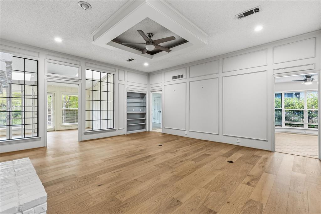 Architectural wainscoting, recessed tray ceiling with integrated ceiling fan, wood-finish flooring, grid-patterned windows, and built-in shelving