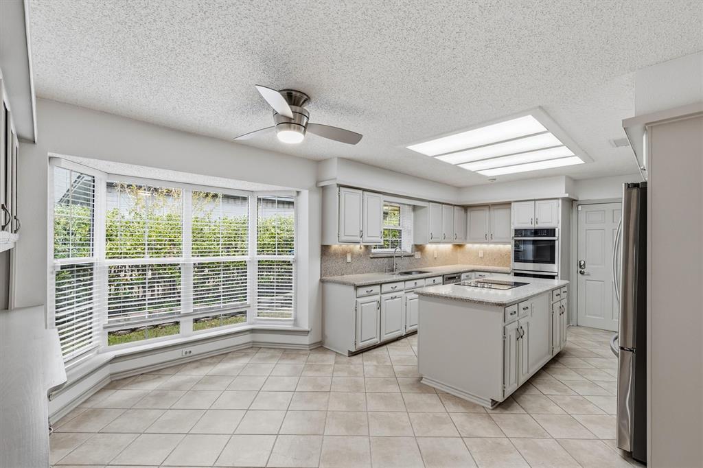 Kitchen featuring a central island with a stone-surface countertop, cabinetry with integrated under-cabinet lighting, built-in double ovens, recessed skylight, and bay windows