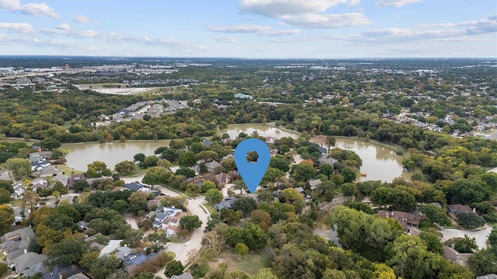 Aerial perspective highlighting a residential lot with mature trees and proximity to a central pond