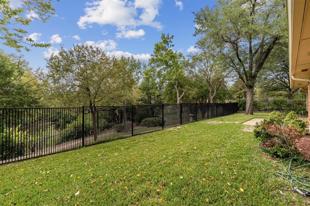 Expansive backyard featuring a manicured lawn, black metal perimeter fencing, and mature trees