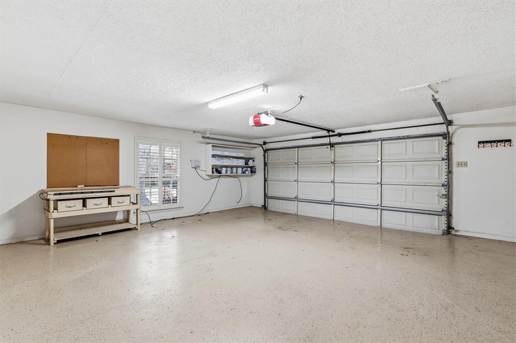 Attached oversized two-car garage featuring a sectional door, high-durability epoxy flooring, fluorescent overhead lighting, and a window with plantation-style shutters
