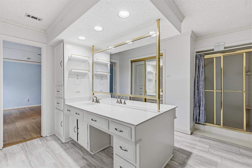 Dual-sink vanity with white cabinetry, light-toned countertop, gold-finish frame mirror, recessed ceiling lighting, and tile flooring