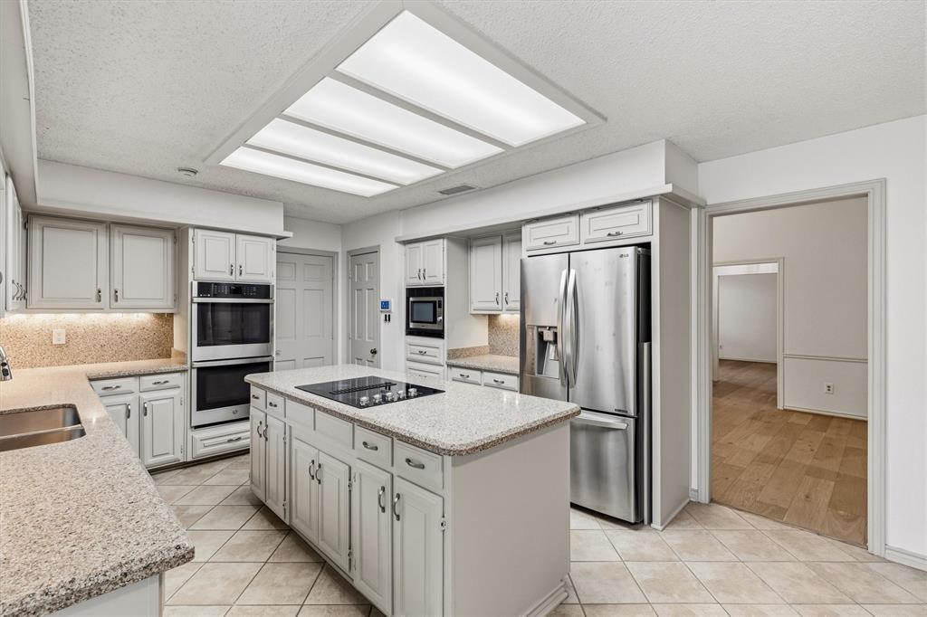 Kitchen featuring light-toned cabinetry, stone-finish countertops, a central island with an integrated cooktop, stainless steel appliances, and tile flooring