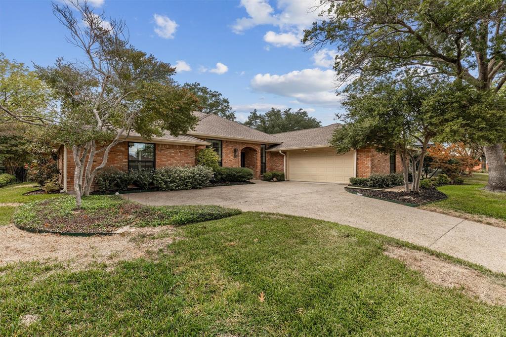 Single-story brick exterior featuring a multi-car attached garage, arched entryway, concrete driveway, and mature landscaping