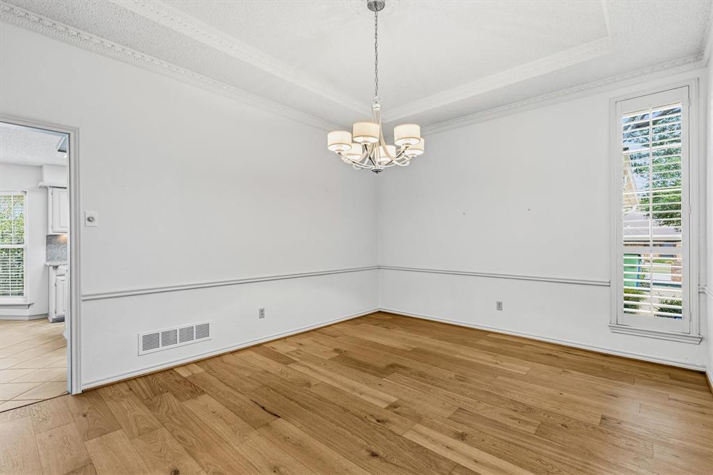 Room featuring wood-finish flooring, a coffered ceiling with crown molding, chair rail detailing, and a multi-arm chandelier with fabric shades