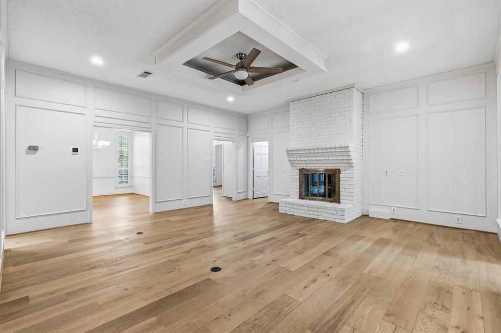 Living area featuring wood-finish flooring, white painted brick fireplace with hearth, recessed tray ceiling with ceiling fan, and extensive wall paneling